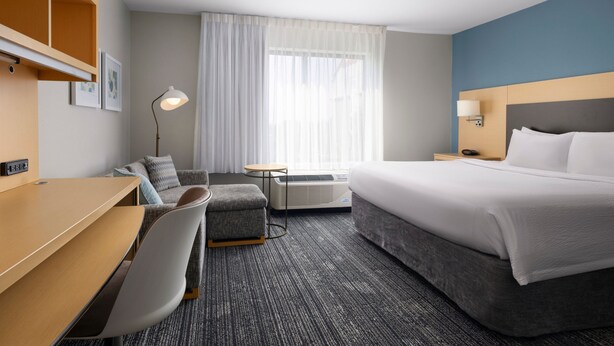 A hotel room with a bed, a desk, a chair, a small table, and a window with curtains. - Towneplace Suites Columbia Northwest/Harbison (Columbia)