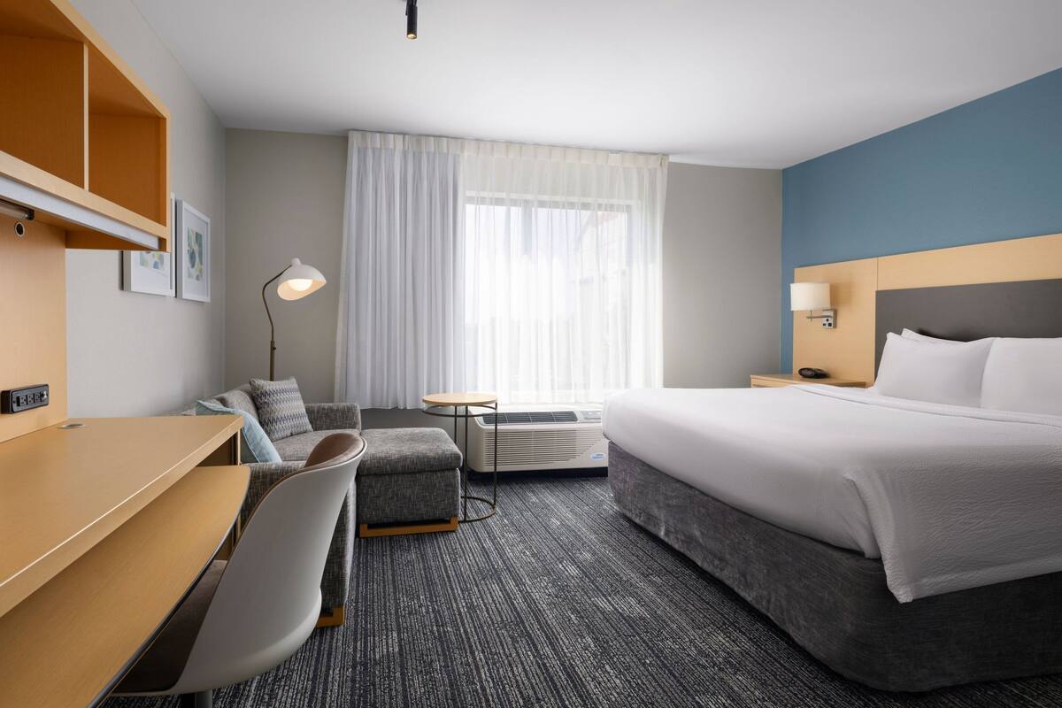 Ein Hotelzimmer mit Bett, Schreibtisch, Stuhl, kleinem Tisch und einem Fenster mit Vorhängen.