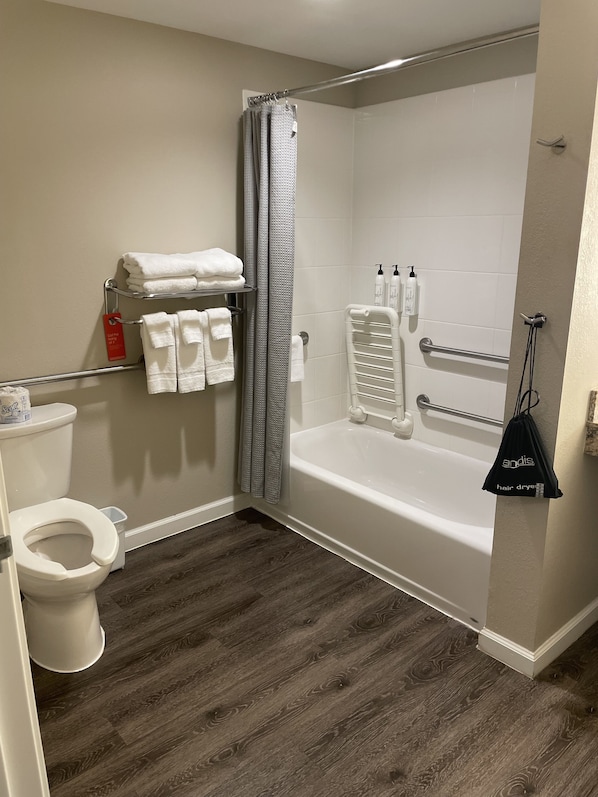 A bathroom with a bathtub, shower, toilet, and a towel rack with folded towels.