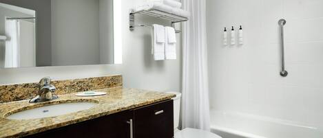 A bathroom with a granite countertop sink, dark wooden cabinet, white toilet, and a walk-in shower with a curtain.