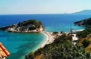 Paisagem costeira com uma praia, afloramentos rochosos e águas azuis cristalinas.