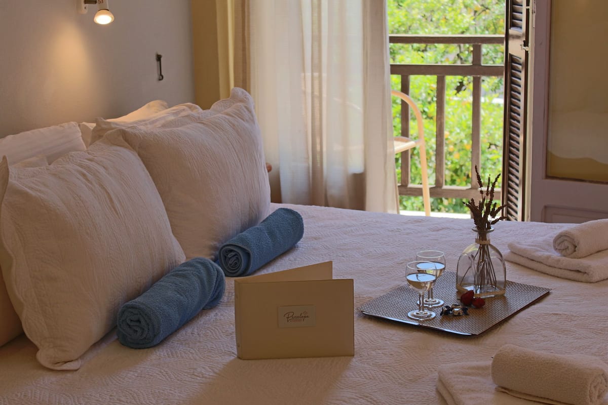 A neatly made bed with white and blue towels, a glass vase with flowers, and a tray with glasses and a card on a textured bedspread.