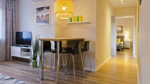 A modern living room with a wooden dining table, black chairs, a TV, and a hanging light fixture. - Aparthotel Apartments Wrocław (Wroclaw)