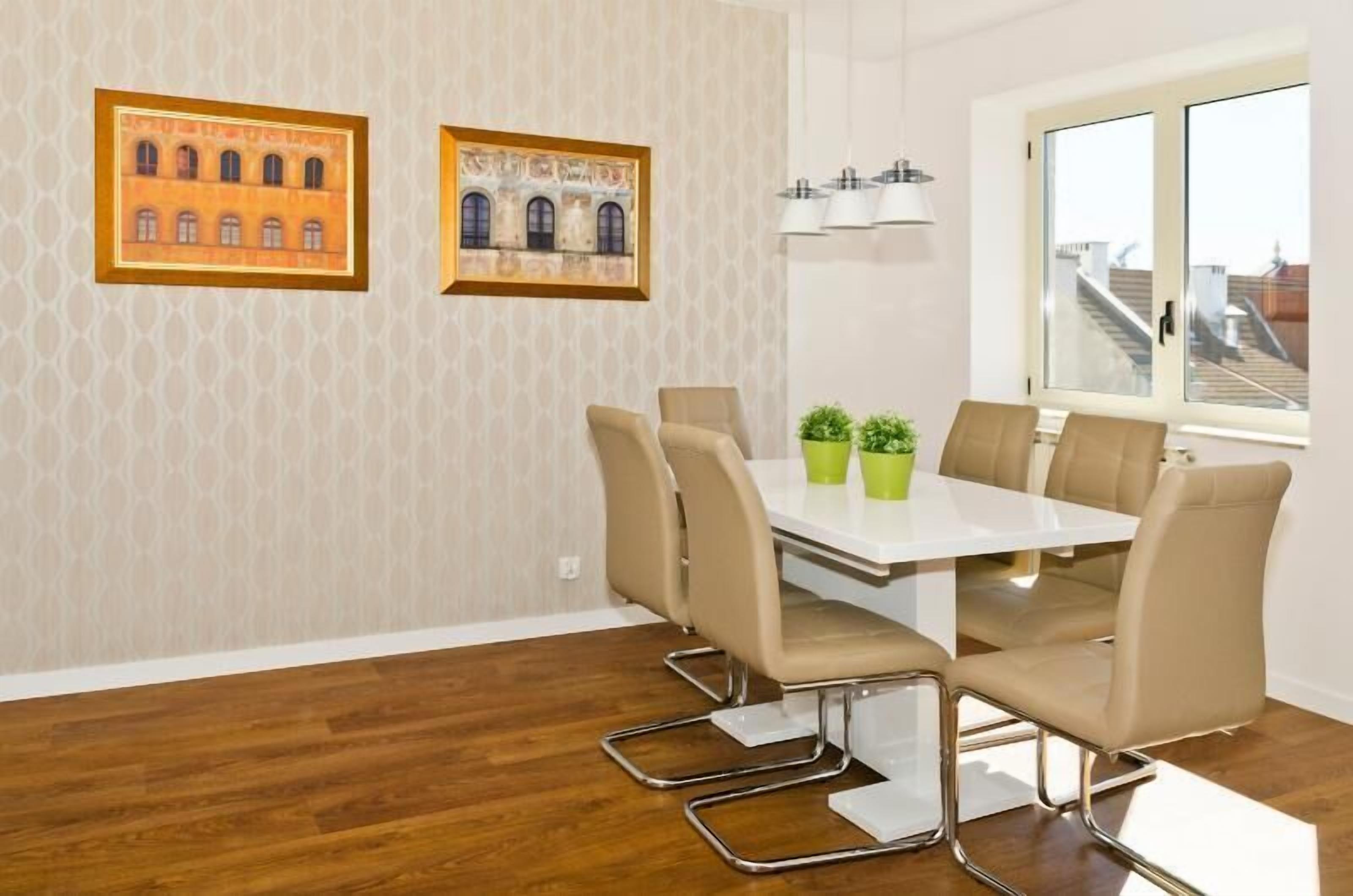 A modern dining area with a white table, beige chairs, and two potted plants.