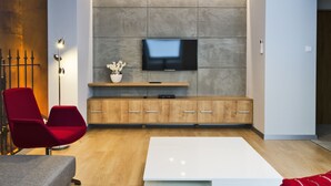 A modern living room with a flat-screen TV mounted on a textured wall, wooden cabinets below, a red chair, and a white coffee table. - Aparthotel Apartments Wrocław (Wroclaw)
