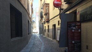 A narrow cobblestone street with a sign for Mahou beer. - Hostal Alcázar (Toledo)