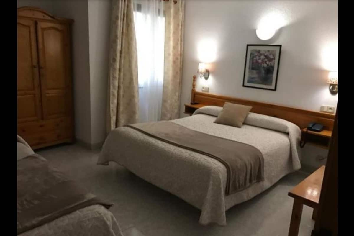 A bedroom with a large bed, a wooden wardrobe, a bedside table with a lamp, and a painting on the wall.