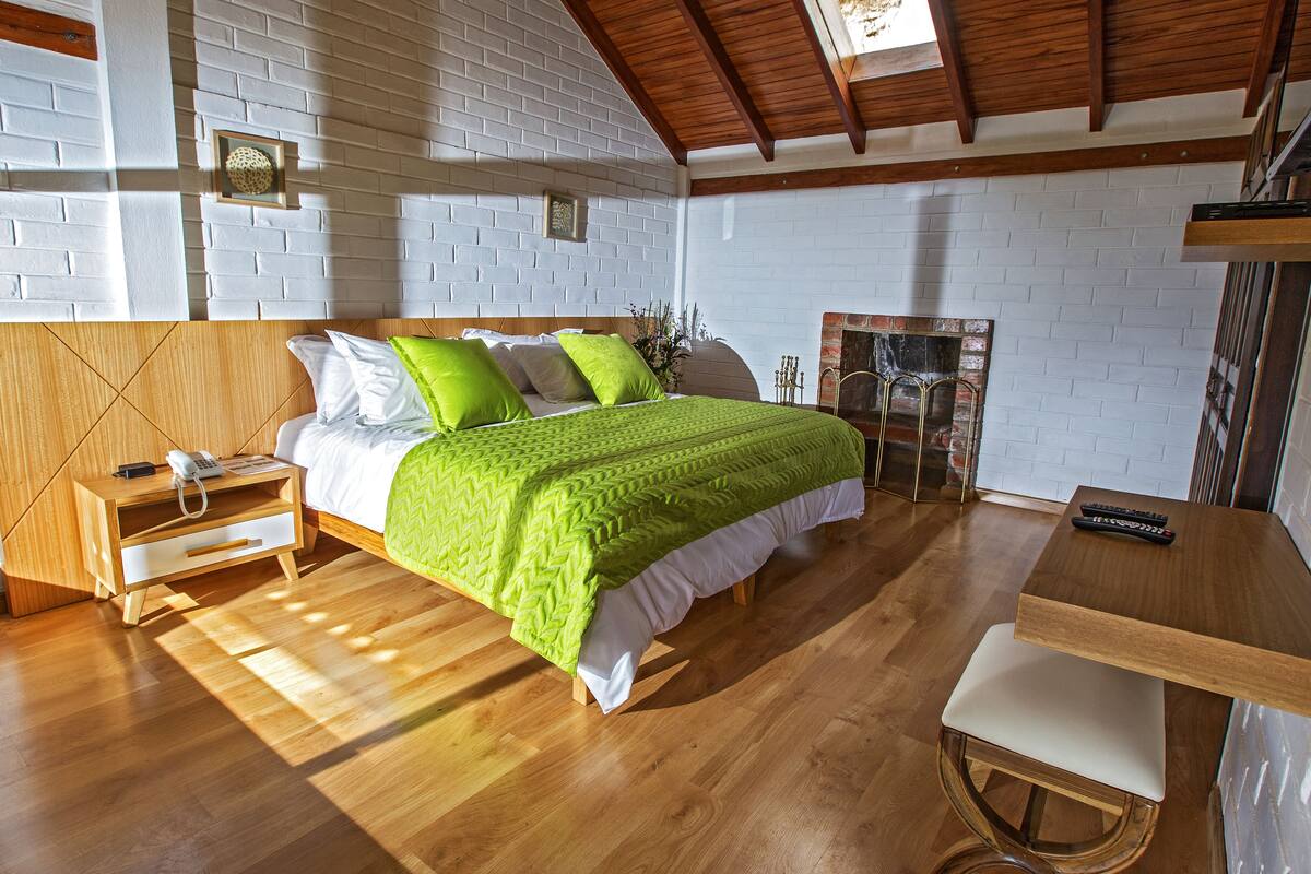 Un dormitorio con una cama de madera, ropa de cama verde y blanca, una mesita de noche de madera y una pequeña mesa con una silla.
