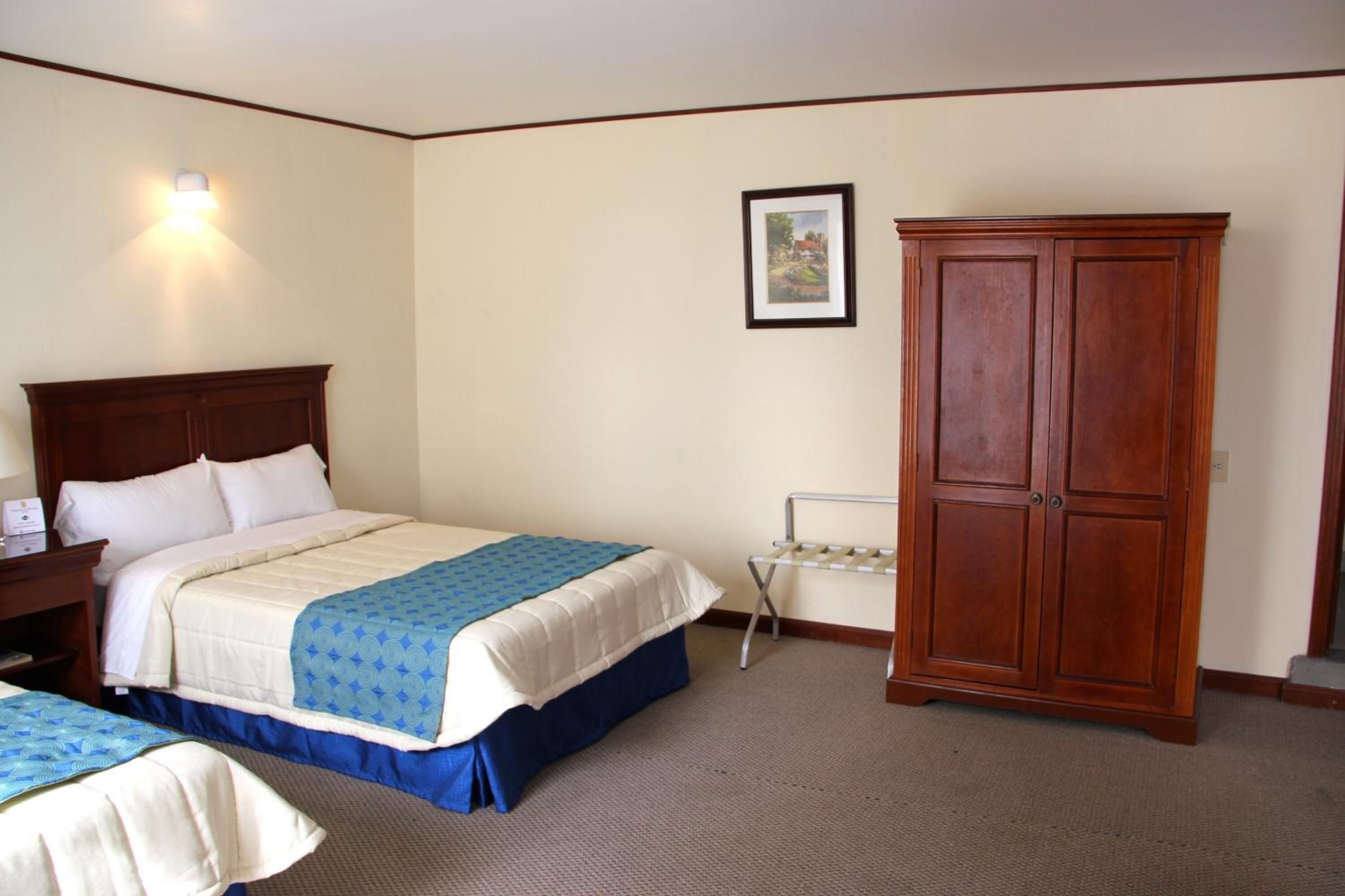 Habitación de hotel con una cama grande, un armario, una mesita de noche y una lámpara en la pared.