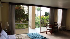 A hotel room with a bed, a chair, a table, and a balcony with a view of greenery. - Hotel Tehuacan Plaza (Tehuacán)
