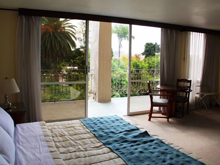 Hotelkamer met een bed, een stoel, een tafel en een balkon met uitzicht op groen.