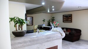 A reception area with a marble counter, potted plants, a telephone, and a couch. - Hotel Tehuacan Plaza (Tehuacán)