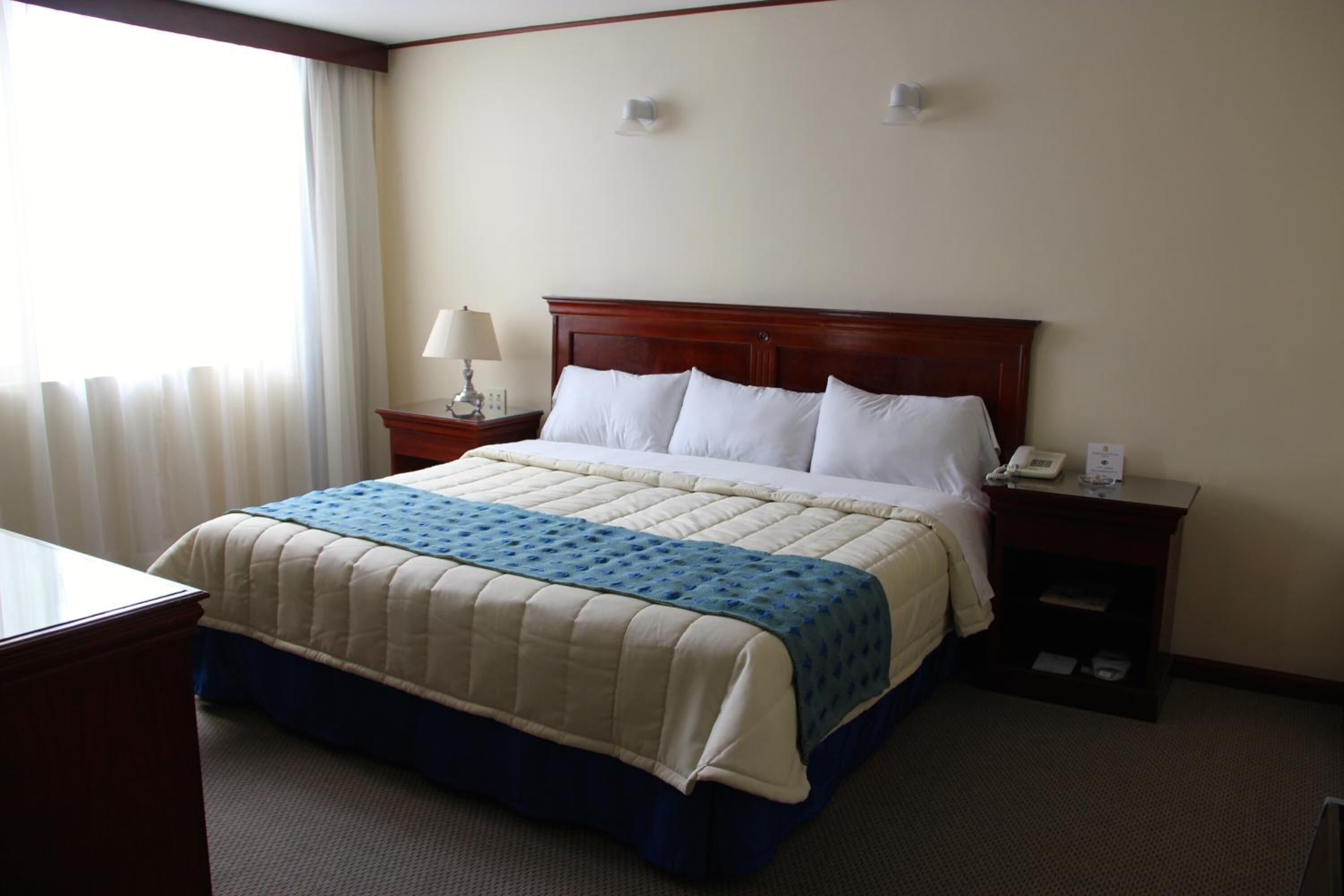 Een hotelkamer met een groot bed, een nachtkastje met een lamp en een raam met gordijnen.