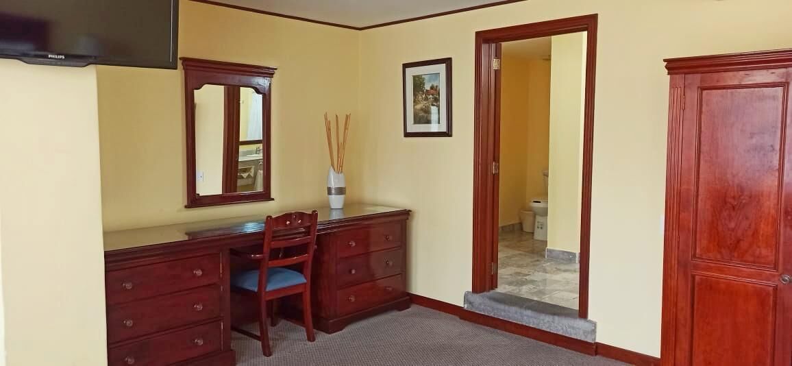 Una habitación con escritorio, silla, armario de madera, espejo y un cuadro en la pared.