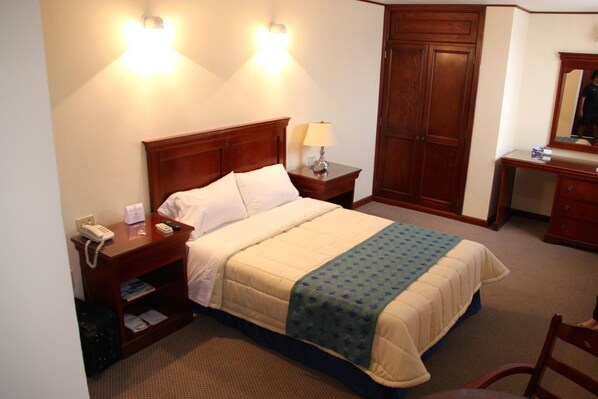 Habitación de hotel con cama, mesitas de noche, lámpara, espejo, armario y una silla.