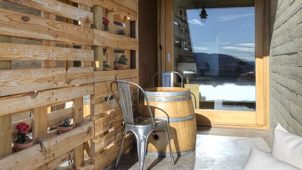 A wooden cabin with a sloped roof, a glass door leading outside, a metal chair, a wooden barrel, and a sofa with cushions. - Trossos del Priorat (Gratallops)