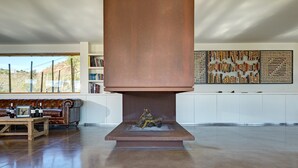 A modern living room with a fireplace, a leather sofa, a coffee table with wine bottles, and a bookshelf. - Trossos del Priorat (Gratallops)