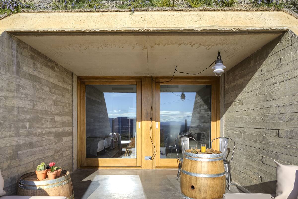 Un área de estar moderna al aire libre, con barriles de madera, una entrada con puerta de vidrio y vistas a la ciudad.