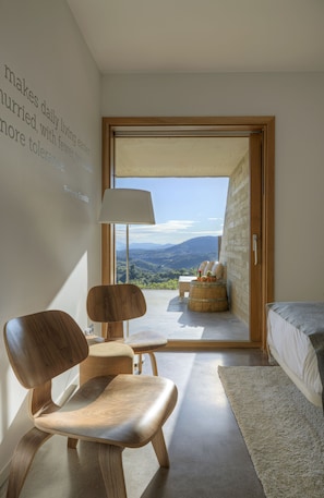 A modern bedroom with a large window, a wooden chair, a bedside table, and a view of the outdoors. - Trossos del Priorat (Gratallops)