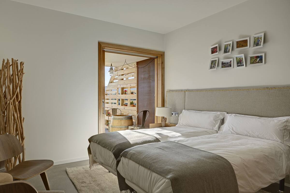 Un dormitorio con una cama, dos sillas, una escultura de madera y una pared con cuadros.