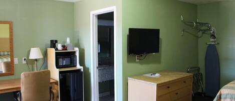 A hotel room with a desk, chair, microwave, television, and a bed with a striped bedspread.