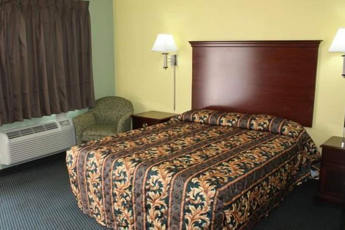 A hotel room with a bed, a chair, a desk, a lamp, and a window with curtains.