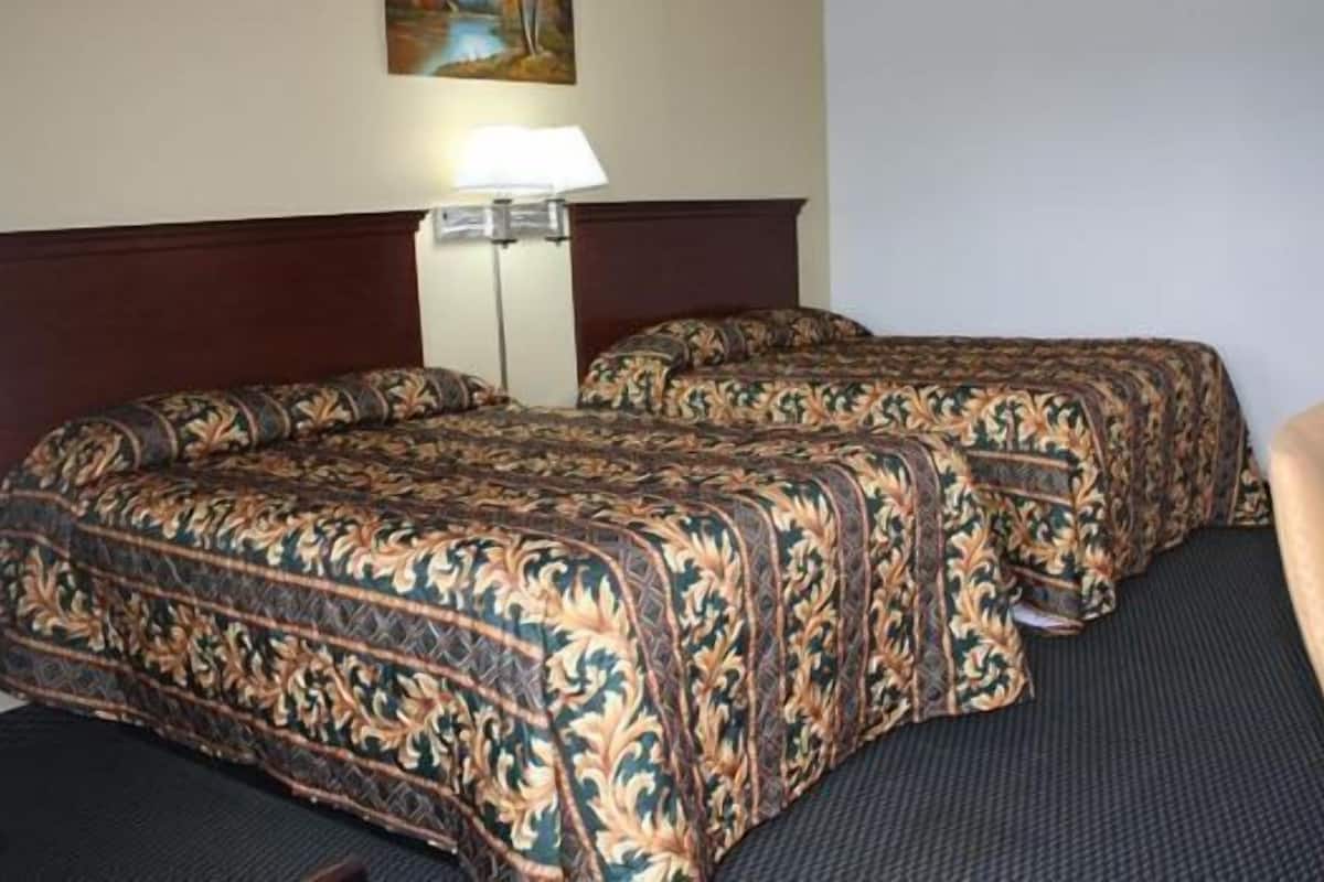 A hotel room with two beds, a desk, and a lamp.