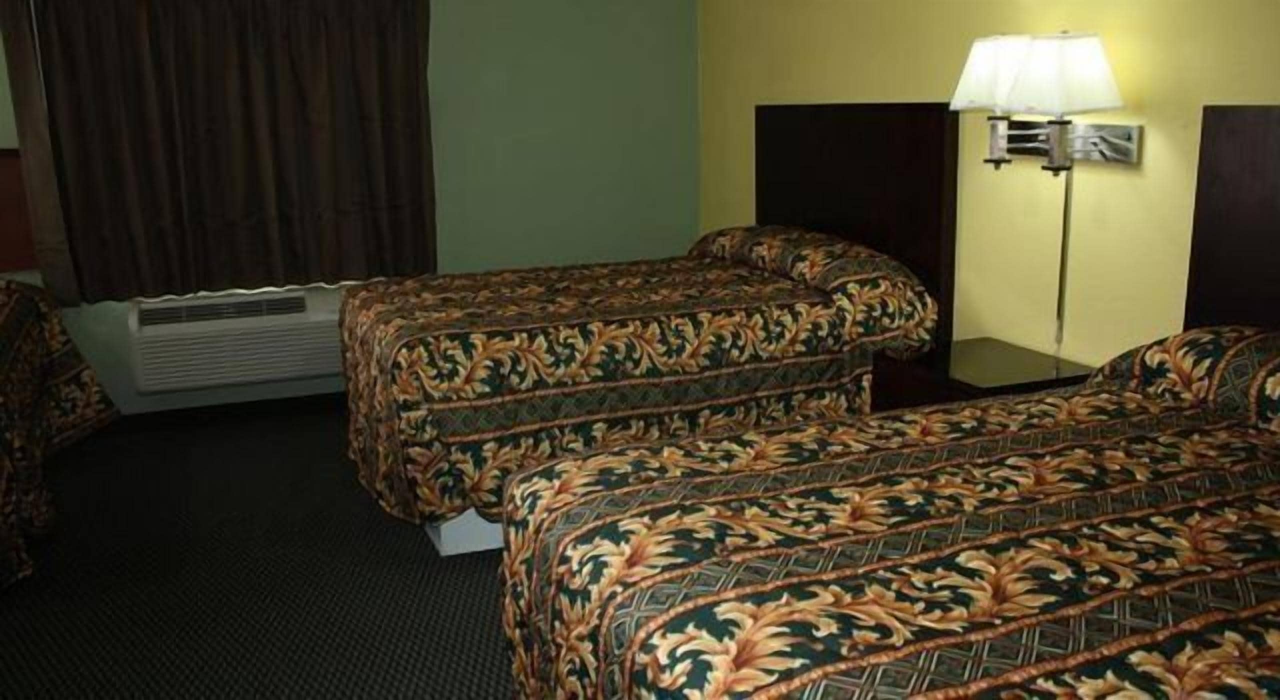 A hotel room with two beds, a heater, a lamp, and a wall-mounted light fixture.