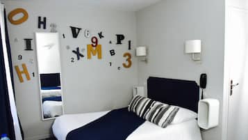 A hotel room with a bed, a mirror, a wall with letters and numbers, a bedside table, a lamp, and a phone.