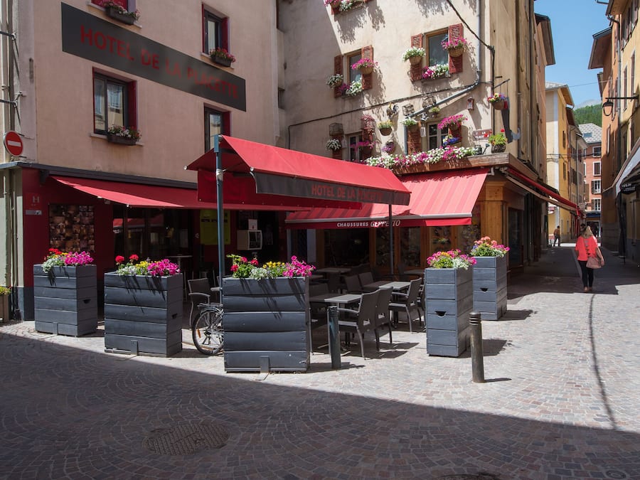 A hotel with outdoor seating, flower boxes, and a cobblestone street.