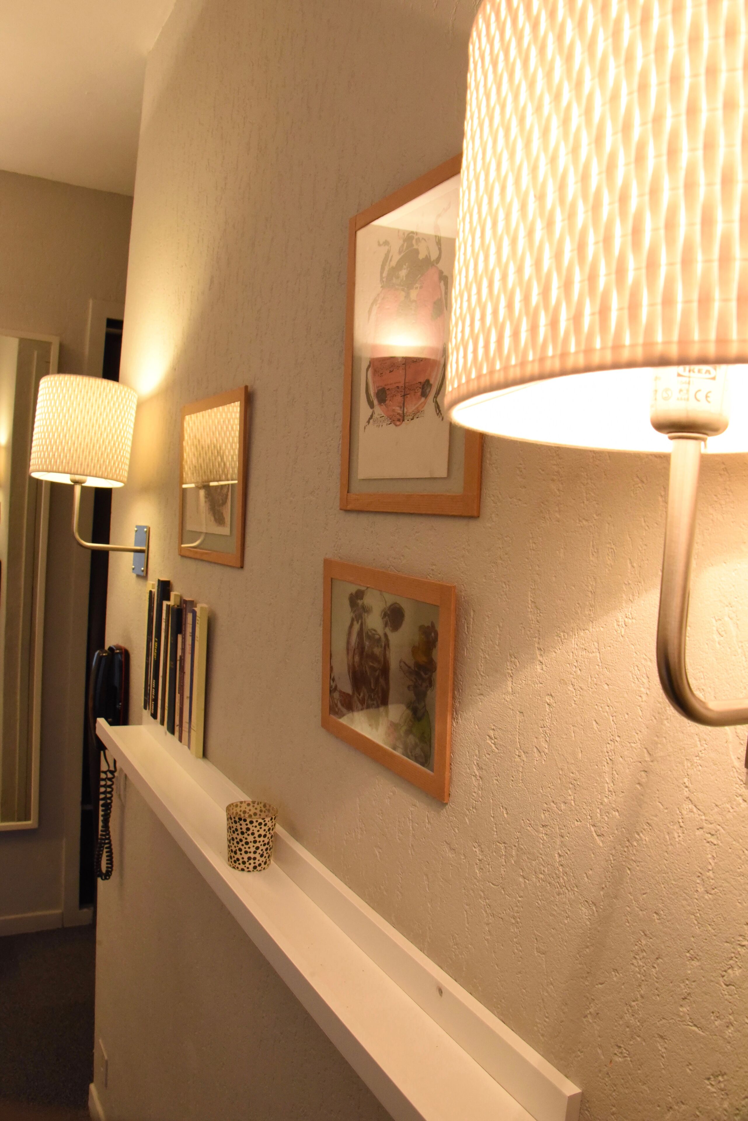 A hallway with a white wall, a white shelf, and three framed pictures.