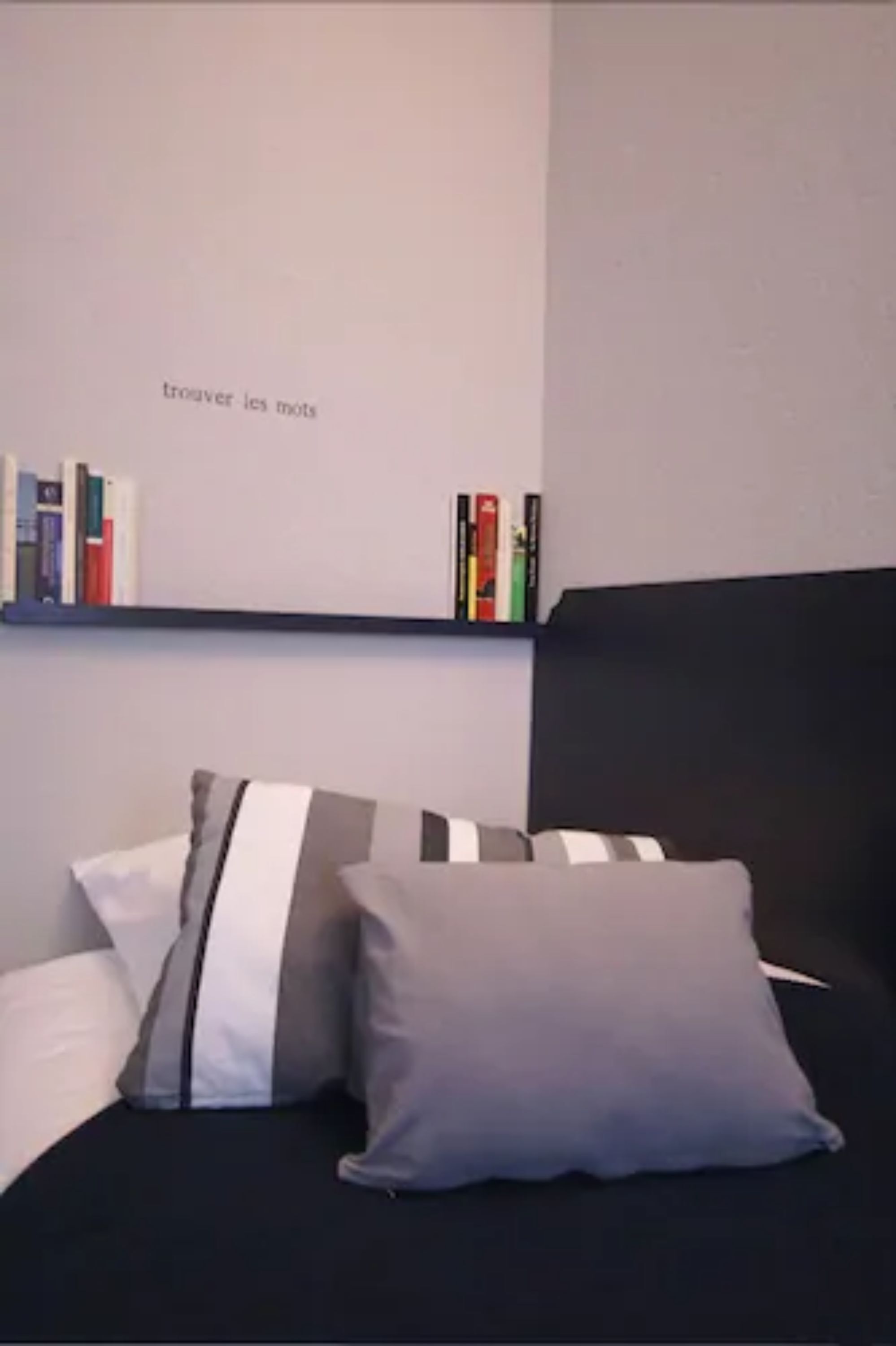 A bedroom with a black headboard, a bed with grey and white striped pillows, and a bookshelf with books and decorative items.