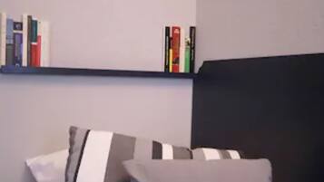 A bedroom with a black headboard, a bed with grey and white striped pillows, and a bookshelf with books and decorative items.