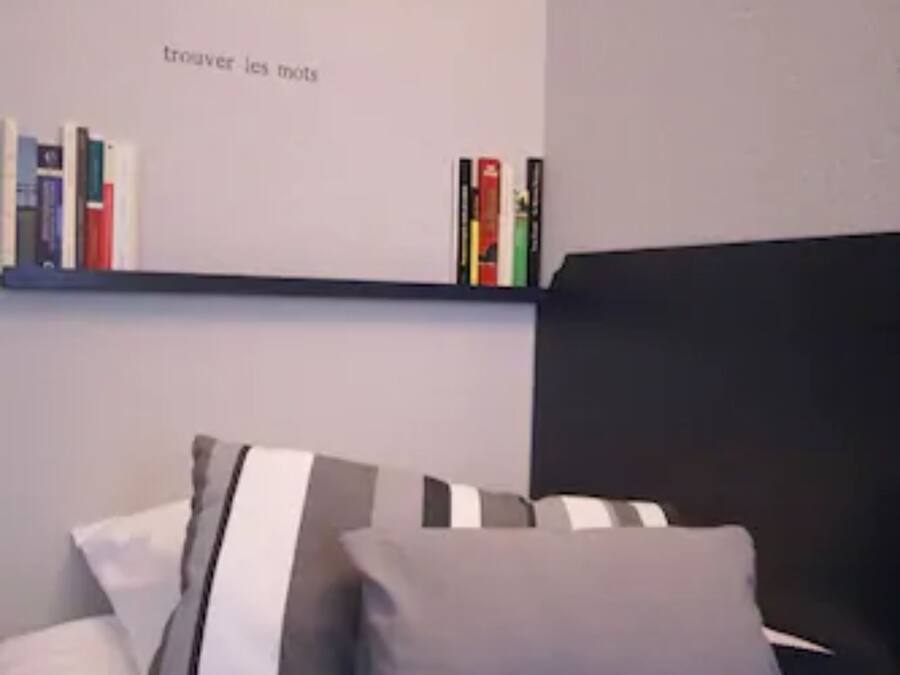 A bedroom with a black headboard, a bed with grey and white striped pillows, and a bookshelf with books and decorative items.