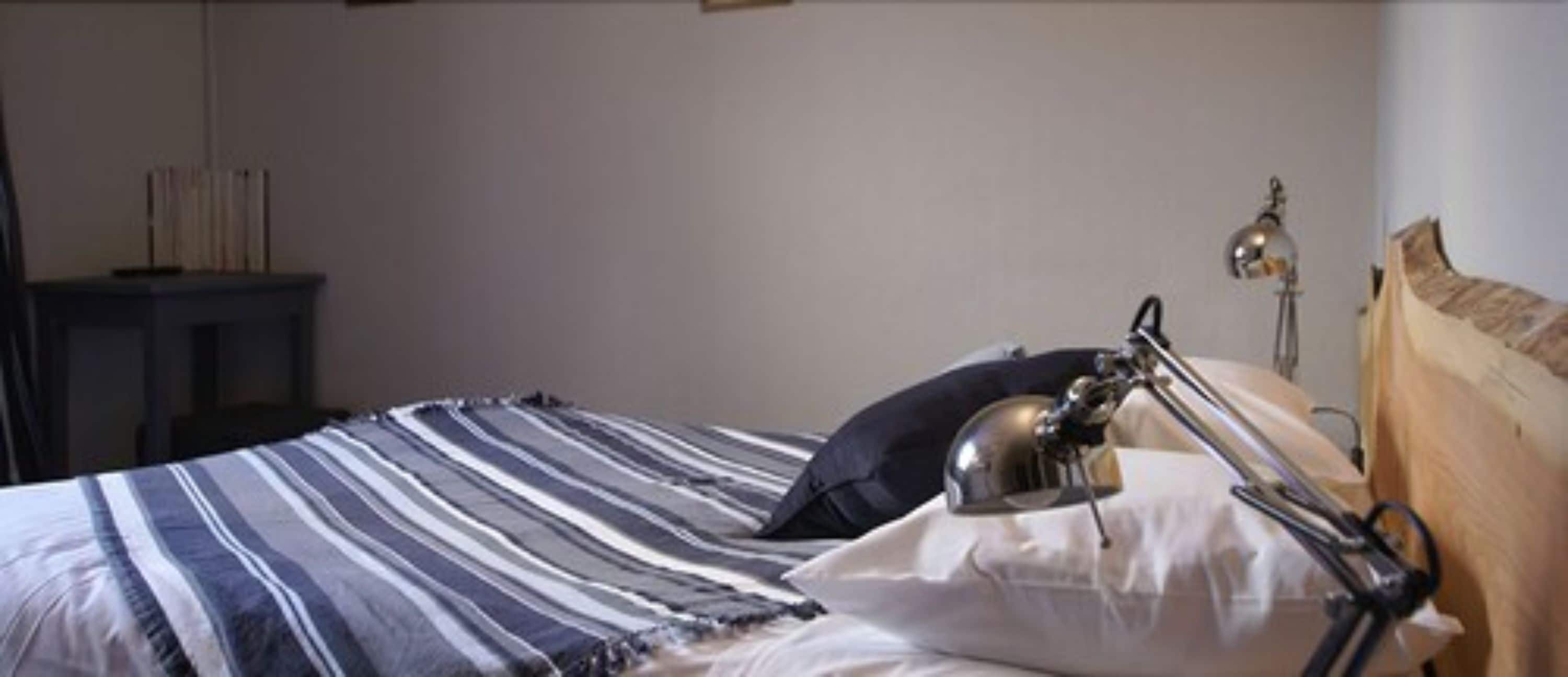 A neatly made bed with striped bedding, a bedside lamp, and a wooden headboard.