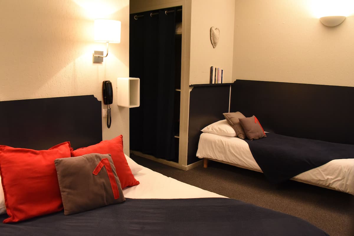 A hotel room with two beds, a phone, a light, and a heart-shaped decoration on the wall.