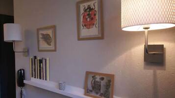 Eine Wand mit gerahmten Kunstwerken, ein Bücherregal und eine Lampe.