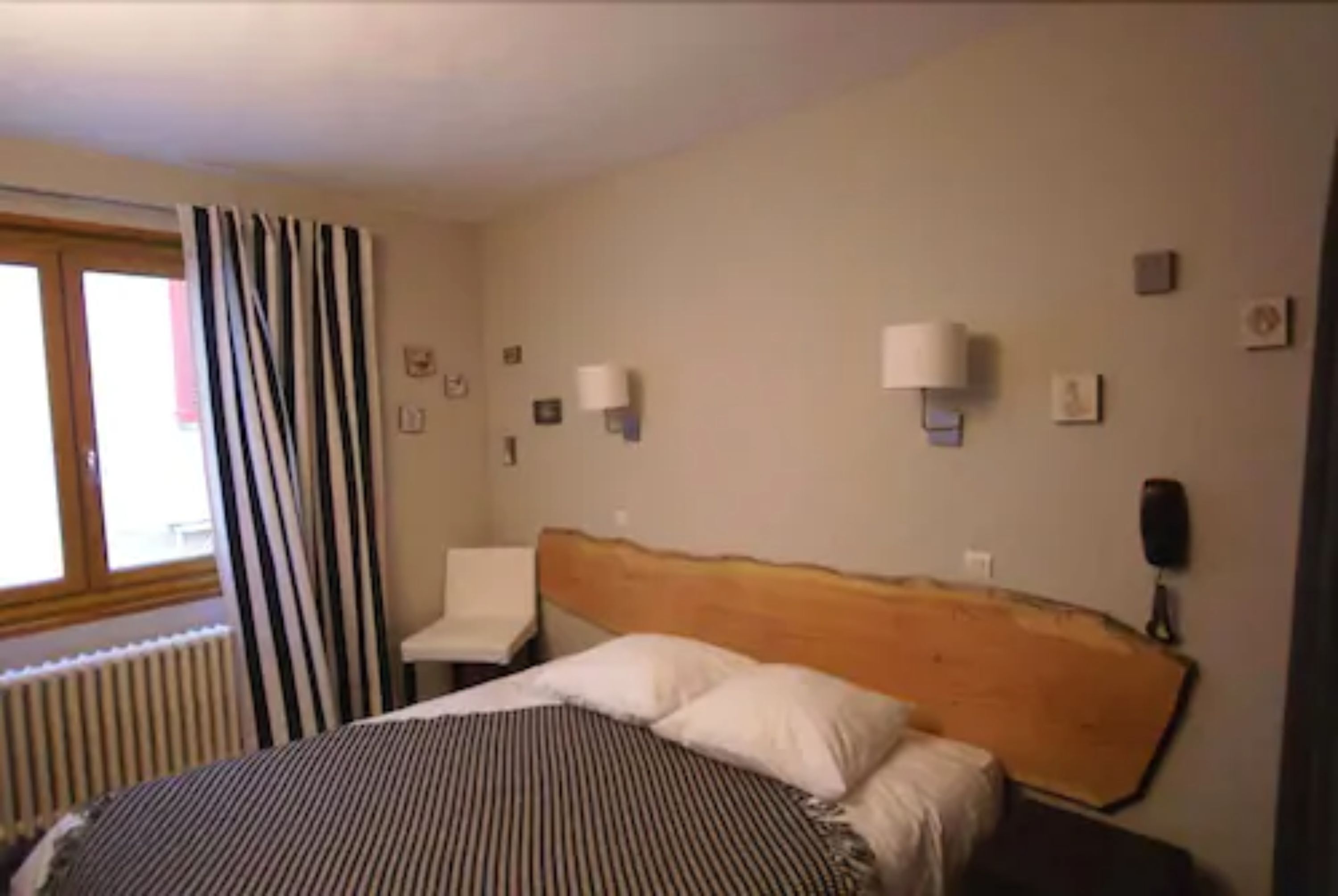 A hotel room with a bed, a nightstand, a lamp, and a window with curtains.