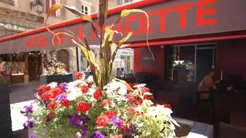 A hotel named "HOTEL DE LA COTTE" with a large sign. In front of the hotel, there is a flower bed with various colorful flowers.