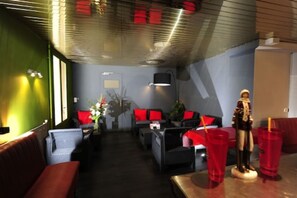 A hotel lobby with a sofa, chairs, a statue, and a table with red cups. - Hotel de La Placette (Barcelonnette)