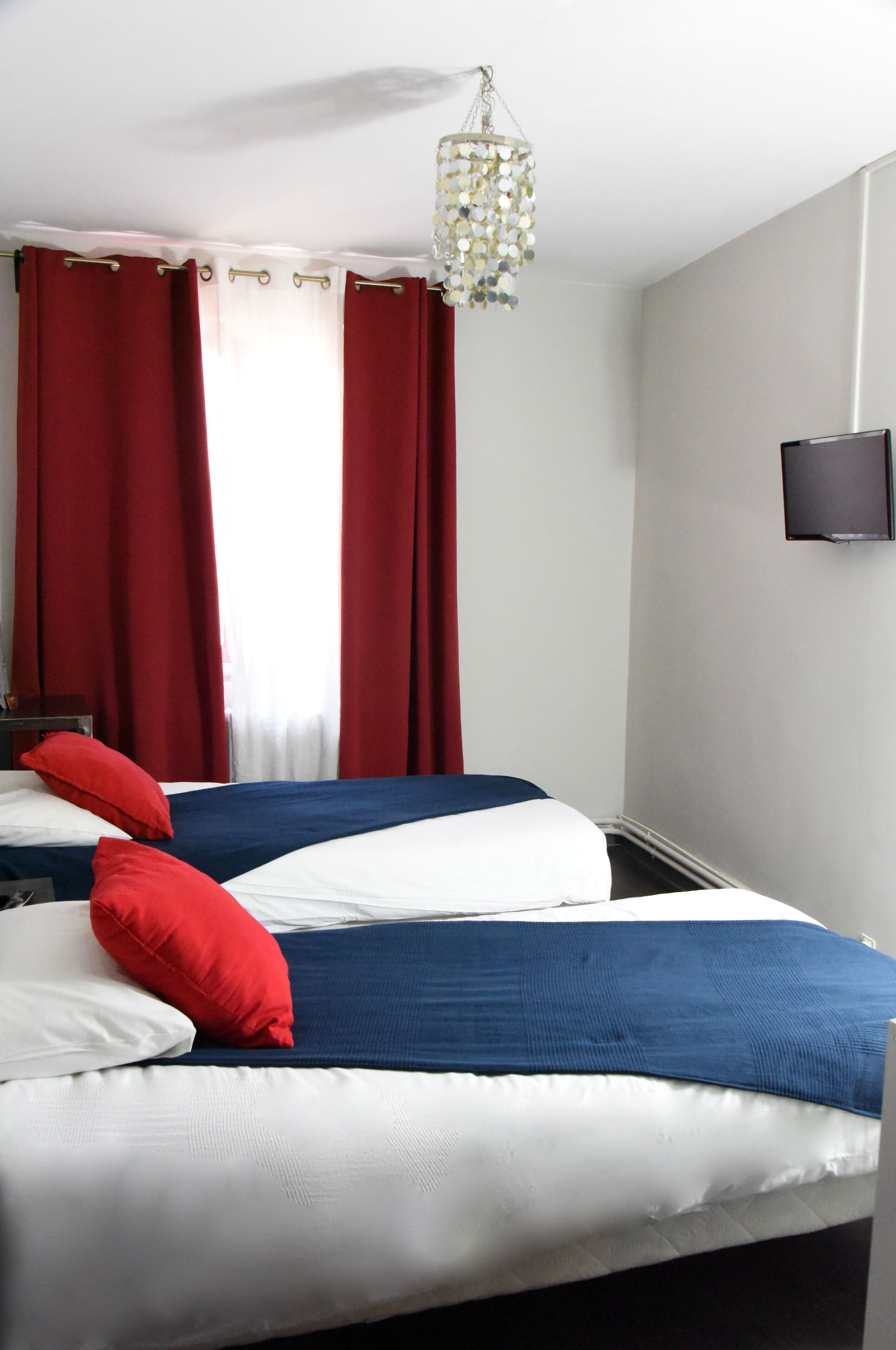 A hotel room with a bed, red curtains, a television, and a hanging light fixture.