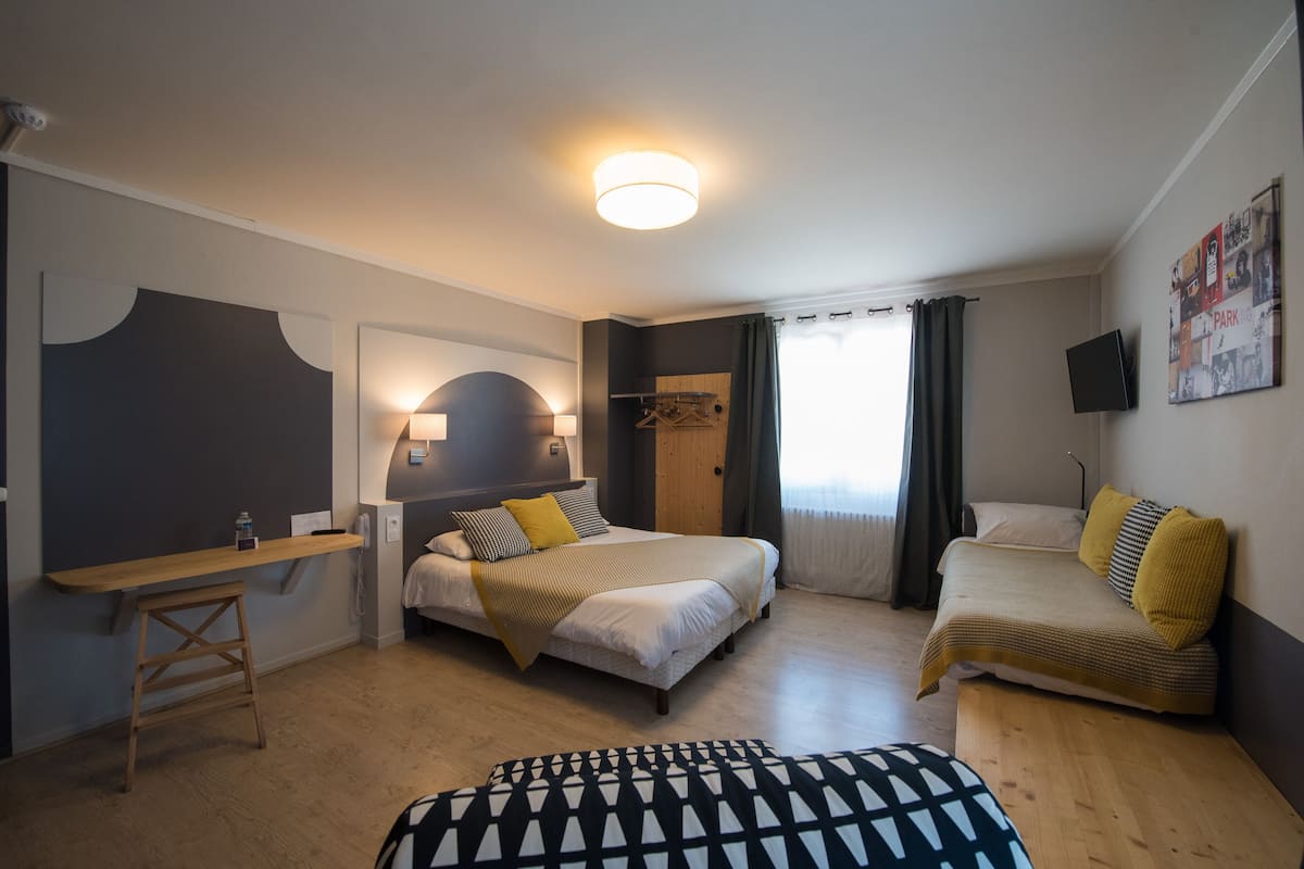 A hotel room with two beds, a desk, a chair, and a TV.