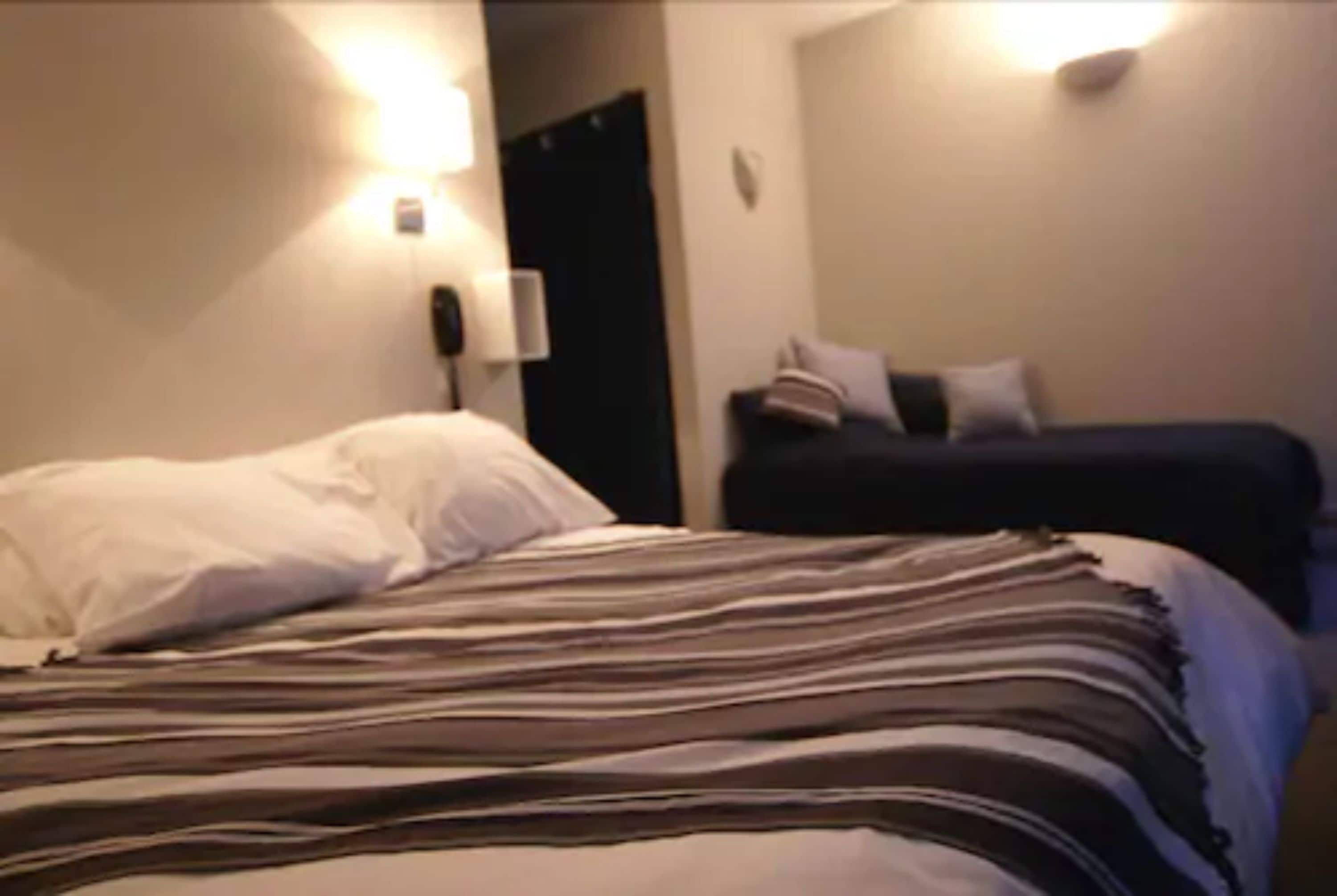 Una camera d'albergo con un letto, un comodino e una lampada a parete.