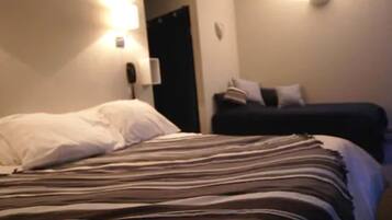 A hotel room with a bed, a nightstand, and a wall-mounted lamp.