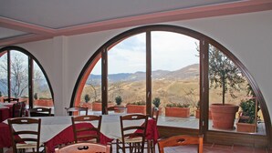 Un restaurante con mesas y sillas, amplias ventanas arqueadas y plantas en macetas.