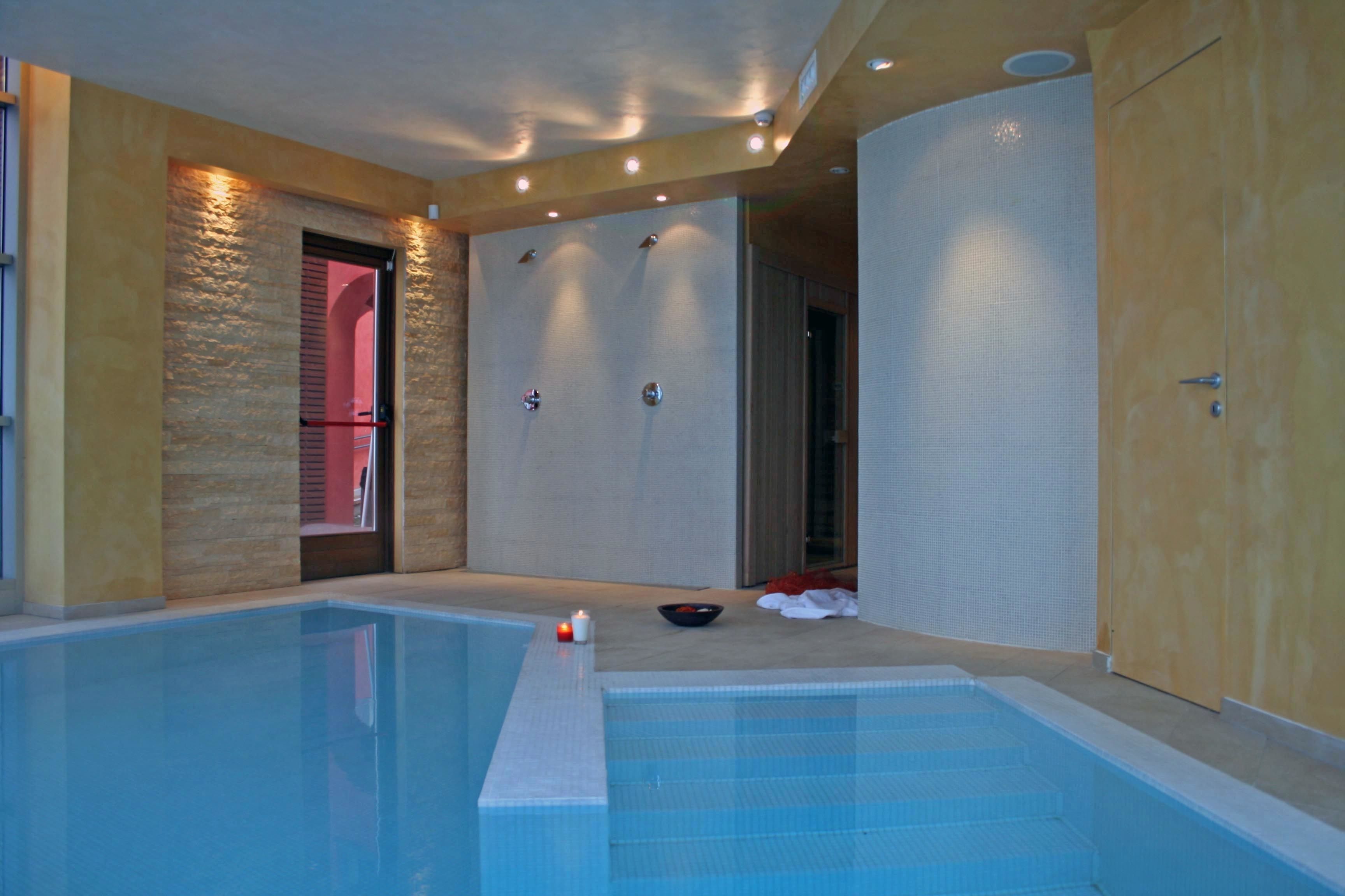 An indoor swimming pool with a tiled floor, a shower area with a glass door, and a towel rack.
