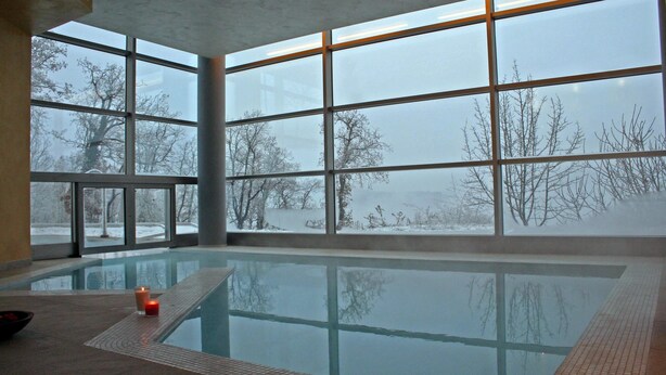 Una piscina interior con amplios ventanales, una vela en el borde y vistas a un paisaje nevado.