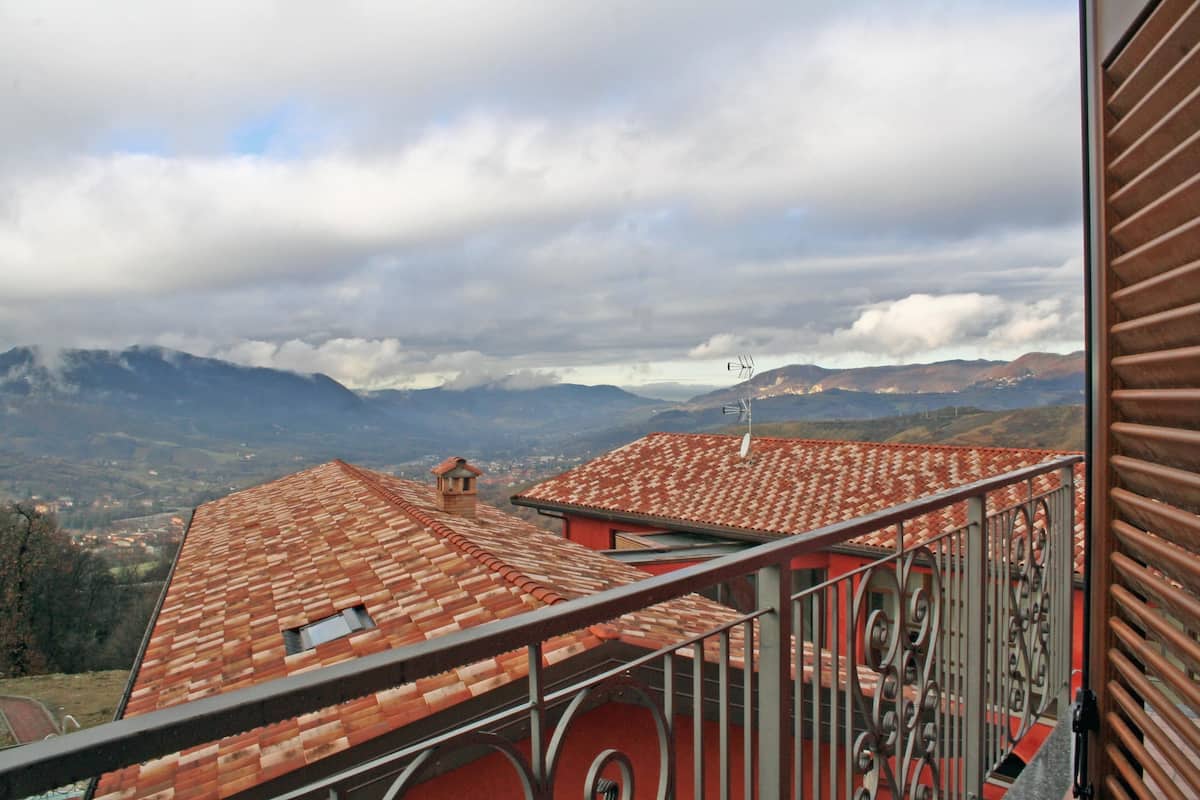 Vista desde un balcón con tejado de tejas rojas, con vistas a un paisaje montañoso.