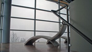 Una escalera moderna con barandilla metálica y piso de madera, que conduce a una habitación con ventanas amplias.
