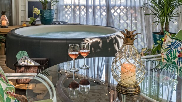 A cozy room with a hot tub, three wine glasses, a candle, and various plants. - Silver Heart Inn and Cottages (Independence)
